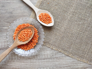 Dried small red lentils in a decorative plate and wooden spoons on a wooden background