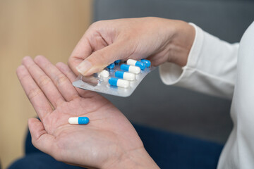 Sick ill asian young woman, girl hand taking tablet pill capsule out from blister pack, painkiller medicine from stomach pain, head ache, pain for treatment, take drug or vitamin at home, health care.