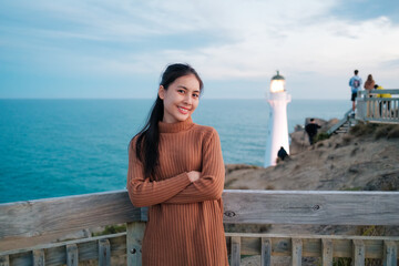 Happy asian woman standing by lighthouse tower on pacific seaside in the evening at Castlepoint