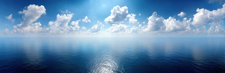 Wide, serene shot of a glassy, dark-blue ocean reflecting the sunny, cloud-filled sky. Sun glare reflects on the water's surface
