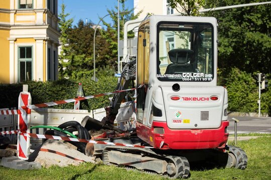Villach, Austria - September 04, 2025: Takeuchi excavator parked on construction site surrounded by safety barriers and green grass, showcasing heavy machinery in urban environment