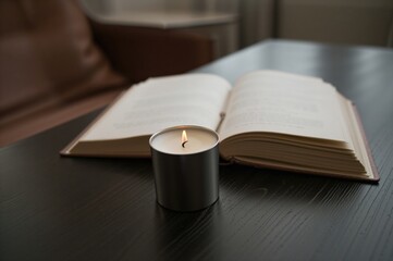 Fototapeta premium A lit candle resting in a holder next to an open book on a surface, photographed with selective focus.