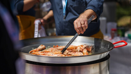 Chef using tongs to cook scampi or nephrops norvegicus in a large pan during a food festival