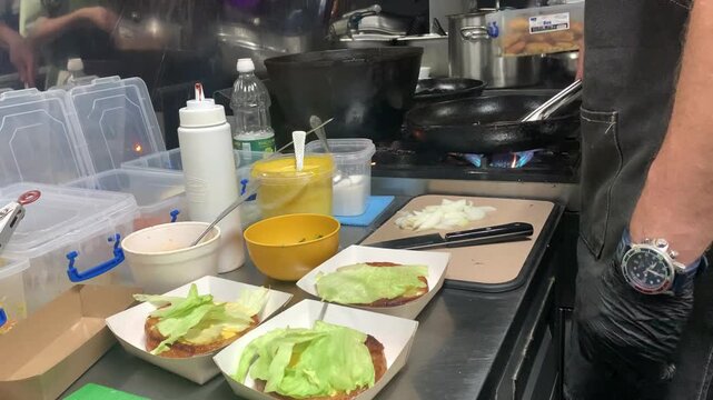 A chef prepares burgers in a cafe kitchen.