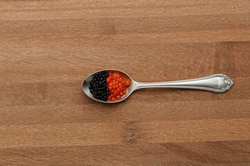 Wooden surface holding a spoon filled with dark and bright orange caviar. Overhead shot with empty space for writing.