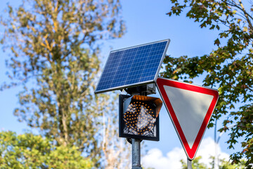 A "Yield" road sign and a traffic light powered by a solar panel against a background of trees.