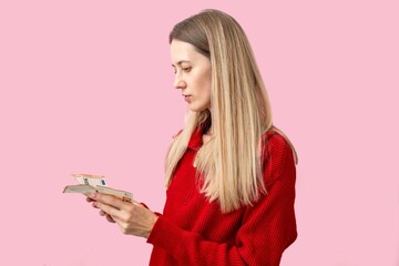 Woman in red sweater counting euro banknotes on pink background