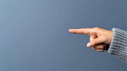 Female hand in gray knitted sweater sleeve pointing right with index finger against blue background, showing direction or choice gesture for business concepts.