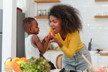 Happy African mother and son making salad while preparing food in the kitchen having fun, mother and son cooking activity concept.