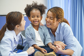 The little girl in curly hair is sitting on the bed in the hospital. The doctor is examining and...