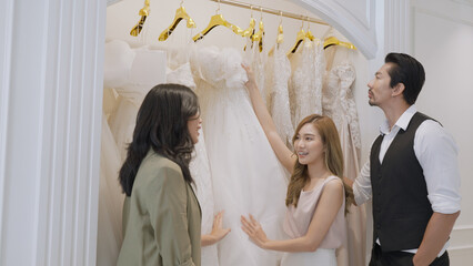 A woman is presenting a wedding dress for couples to choose from at wedding dress shop.