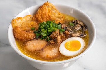 A steaming bowl of noodles in a rich golden broth garnished with crispy chicken tempura, soft-boiled egg, seaweed, mushrooms, and chopped green onions.