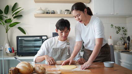 Happy couple rolling dough with a rolling pin while baking together in a cozy kitchen.
