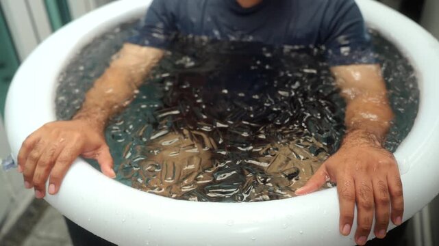 Close-up Man practices cold therapy and ice bathing in inflatable tub, using Wim Hof Method for wellness, meditation, fitness recovery, sports therapy. Wellness and healthy.
