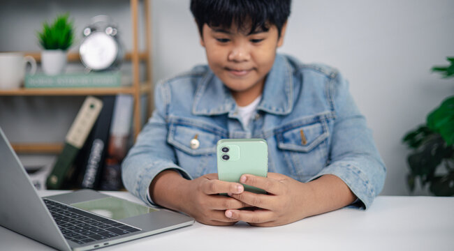 Asian boy using smartphone and laptop for online learning and digital lifestyle concept