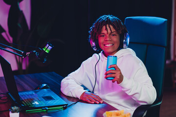 Cheerful teenage streamer with microphone and energy drink recording live in a high-tech gaming setup at home