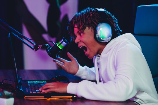 Teen boy streaming online using a microphone and headphones in a modern setup with neon lights, showcasing gaming and vlogging passion