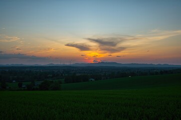 Fototapeta premium Silhouetted hills and lush meadows under a sunset sky