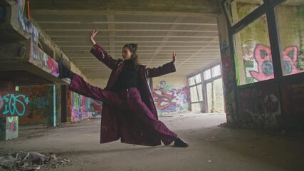 Stylish woman dances elegantly in abandoned building covered in graffiti