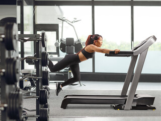 Fototapeta premium Scared young woman trying to run fast on a treadmill