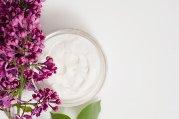 Creamy skincare product surrounded by vibrant lilac flowers on a neutral background in a serene setting