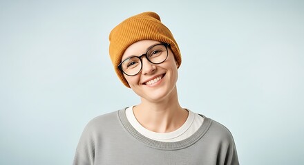 A young woman with short hair, wearing a mustard yellow beanie and round glasses, smiles warmly against a light blue background.