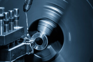 The lathe machine finish cut metal shaft parts with liquid coolant method in the blue tone scene.