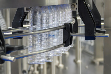 The  empty drinking water bottles  hanging on the overhead conveyor belt for filling process.