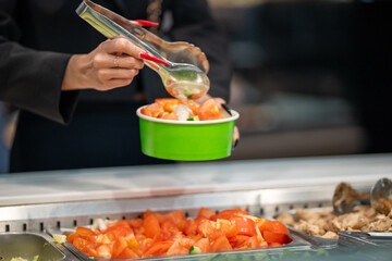 A close-up of a woman's hands with long red nails using metal tongs to serve food at a Weight-Pay cafeteria