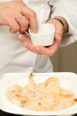 Chef de cozinha preparando um prato da culinaria mediterranea, com camaroes fritos no azeite, vinho branco e temperos
