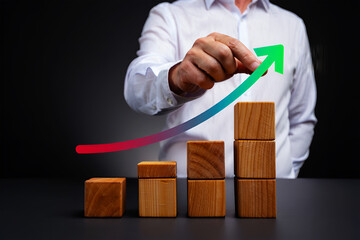 Person hand draws upward arrow graph over wooden blocks drawing