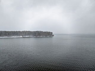 November landscape with covered with first snow birch and spruce forest on lake shore. First snow on lake.