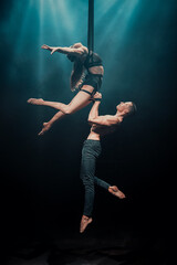 Male and female aerial duo performing on straps. The man supports the woman as she arches gracefully mid-air under dramatic blue stage lighting. Horizontal image. © Dima
