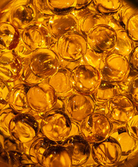 Omega-3 capsules of fish oil close-up, golden background, creating a shiny texture and warm glowing surface. The pattern of vitamin supplements highlights health, nutrition, and wellness.