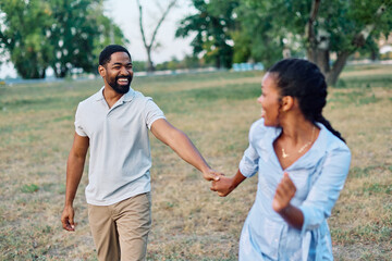 Happy active young black  couple having fun walking running holding hands and bonding in park or nature outdoors