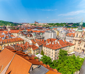 Obraz premium An aerial view across the rooftops towards the distant castle complex from the City Hall tower in the old town square in central Prague in springtime