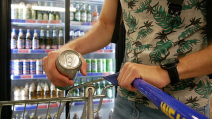 Close-up of male customers hand putting a cold beer can in a shopping cart