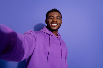 Obraz premium Portrait of a smiling young man in a purple hoodie posing against a vibrant violet background, showcasing casual style