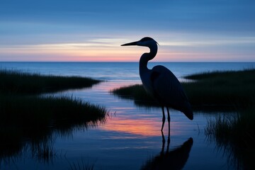 Silhouette of heron standing in calm water at sunset with colorful sky and reflections, surrounded by marsh grass and serene ocean background. Ai generative