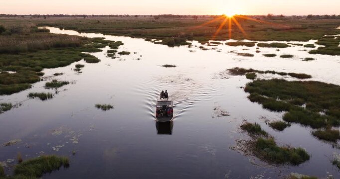 High aerial. Tourists on a sightseeing boat on a river in the Okavango Delta at sunset