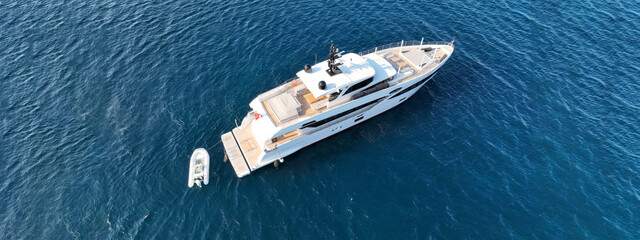 Aerial drone ultra wide top down photo of luxury yacht with wooden deck anchored in deep blue sea of Mykonos island, Cyclades, Greece