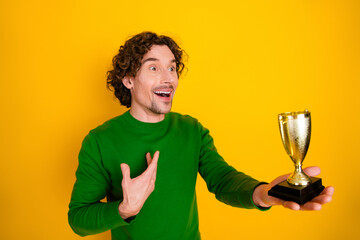 Joyful man holding a golden trophy on a vibrant yellow background, showcasing excitement and...