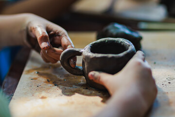 Close up of child hands sculpting clay pottery mug. Kid making clay cup handcraft workshop for hobby activity.