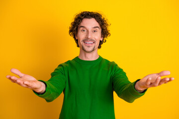 Happy young man in green sweater with outstretched arms standing against a yellow background, conveying warmth and positivity