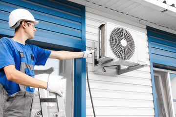 Caucasian male technician installing outdoor air conditioning unit on building.