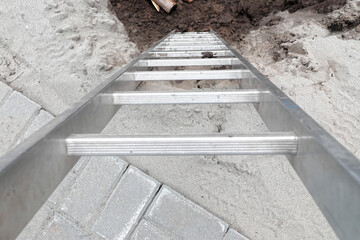 Metal ladder on sandy construction site with paving bricks.