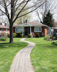 A charming brick house with a winding pathway surrounded by lush green grass and trees, creating a welcoming atmosphere.