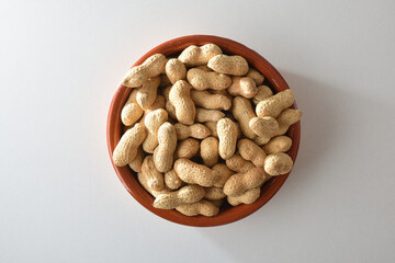 Heap of peanuts with skin in clay bowl on table