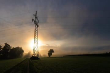 Freileitungsmast bei Sonnenaufgang im Morgennebel