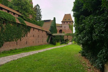 Historic brick castle walls covered in greenery with a grassy path leading toward a tower in a serene setting